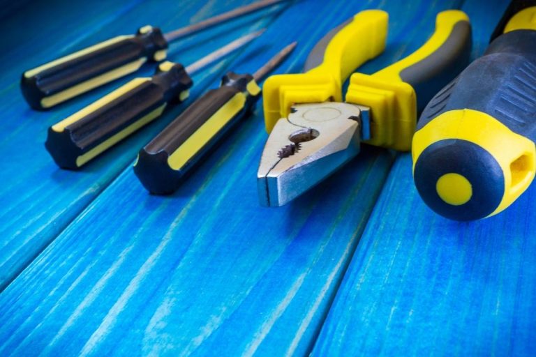 A variety of tools arranged on a blue wooden table, including a hammer, screwdriver, and pliers.
